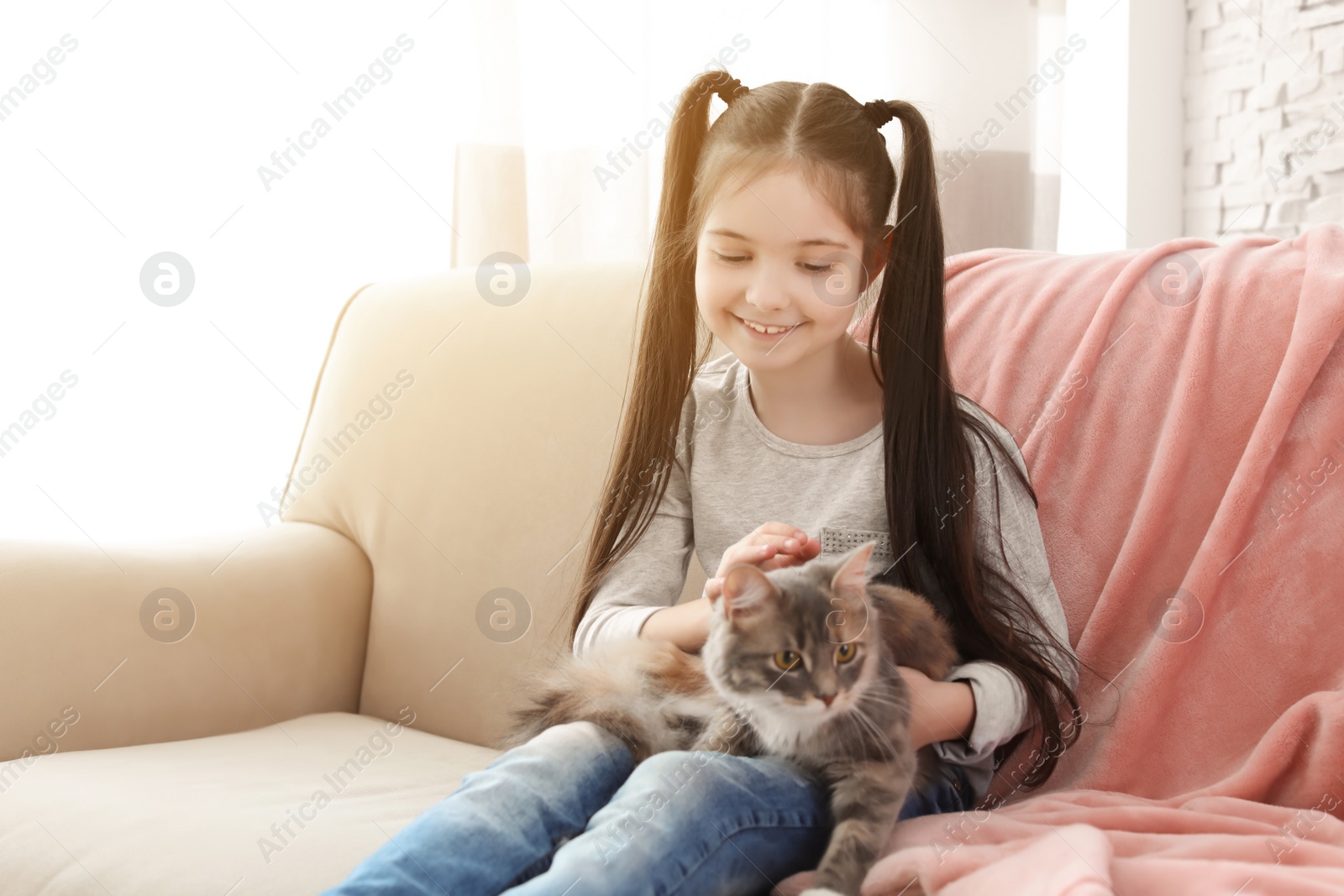 Photo of Cute little girl with cat sitting on sofa at home