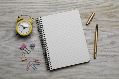 Ballpoint pen, notebook and different clips on wooden table, flat lay