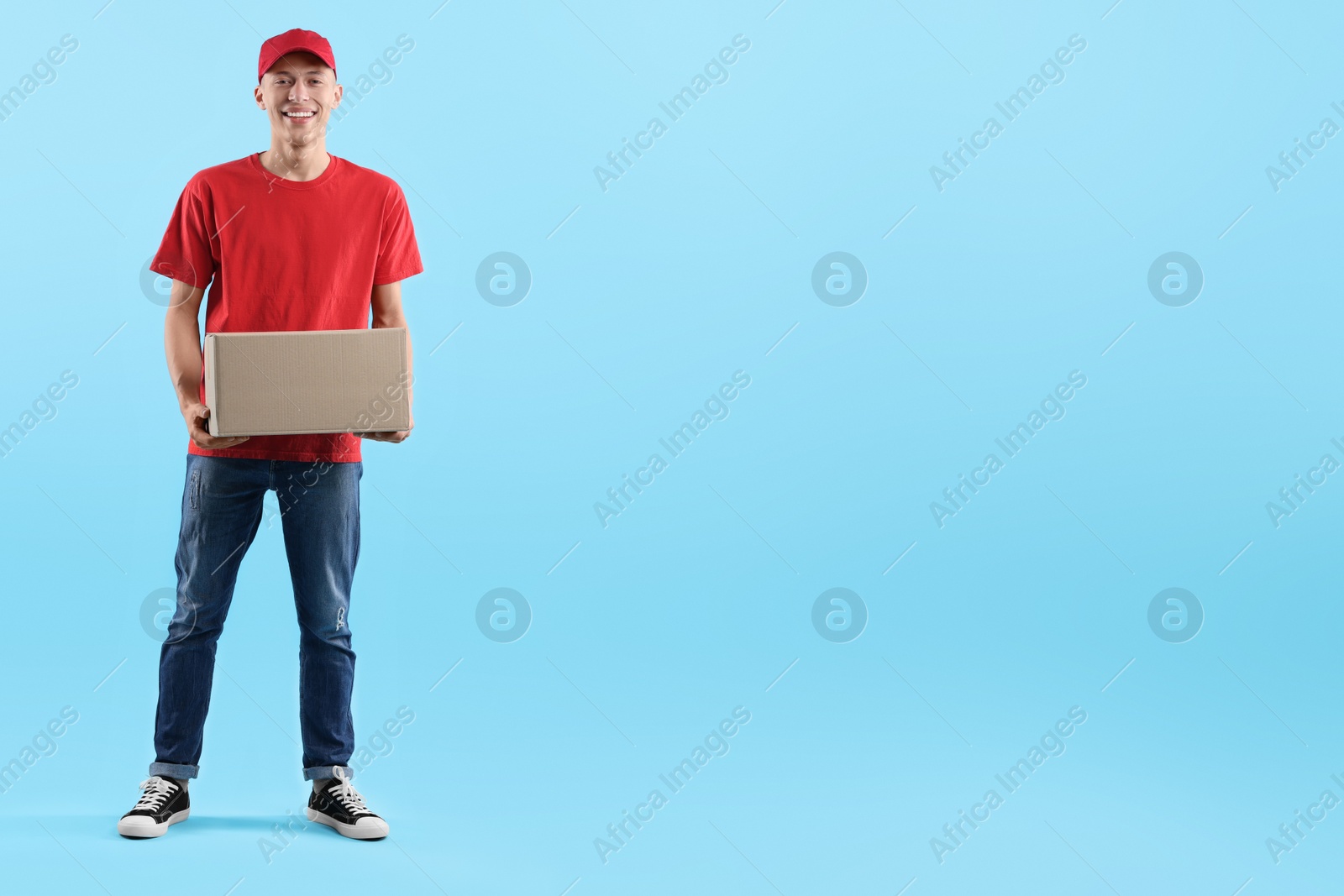 Photo of Happy courier with parcel on light blue background. Space for text