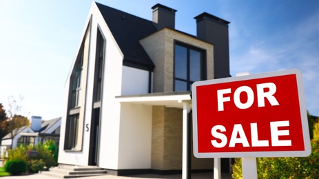 Photo of Red real estate sign near house outdoors on sunny day