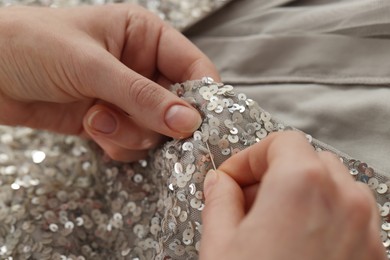 Photo of Dressmaker sewing party dress from silver fabric with paillettes at table in atelier, closeup