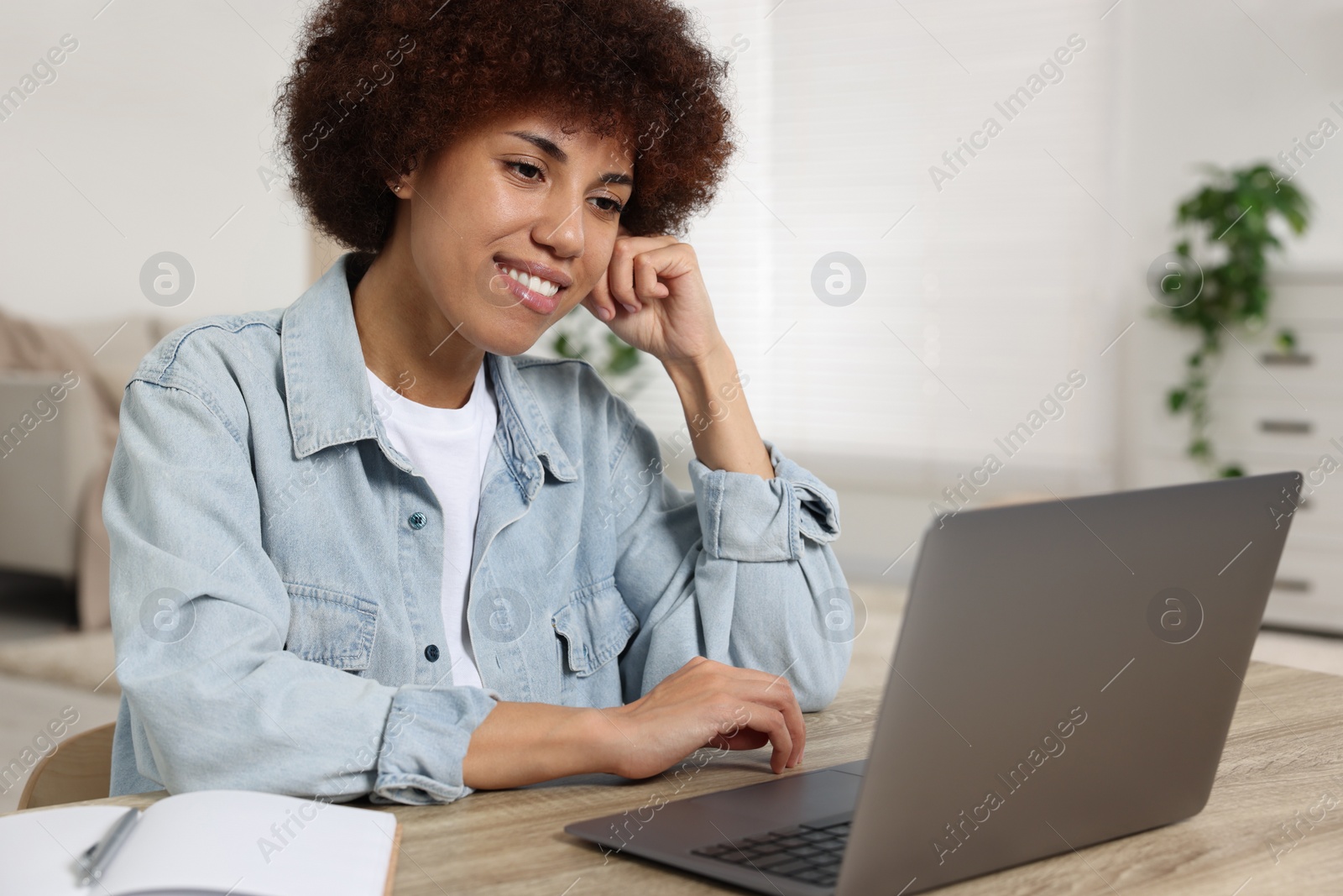 Photo of Young woman using laptop at wooden desk in room