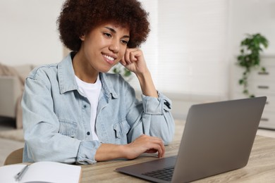 Photo of Young woman using laptop at wooden desk in room