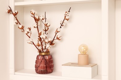 Shelf with fluffy cotton flowers and different decor near beige wall. Interior design