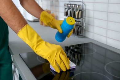 Photo of Male janitor cleaning kitchen stove with sponge, closeup