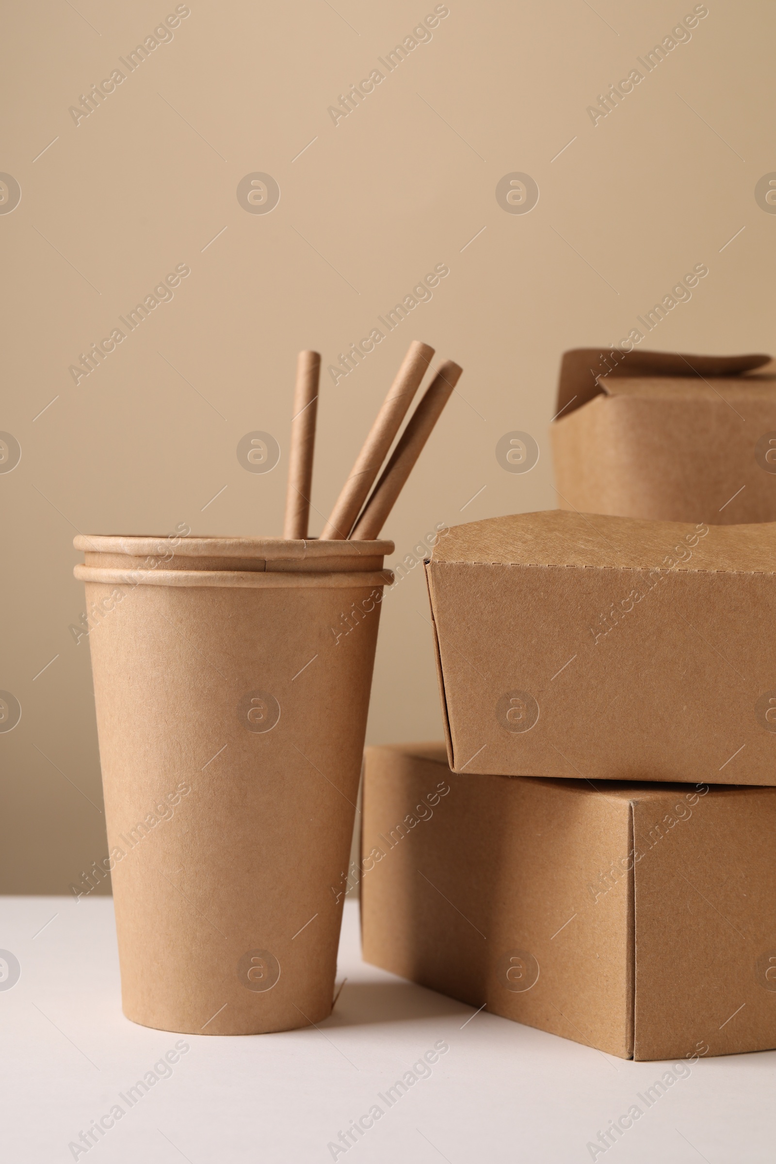 Photo of Eco friendly food packaging. Paper containers and straws on white table against beige background