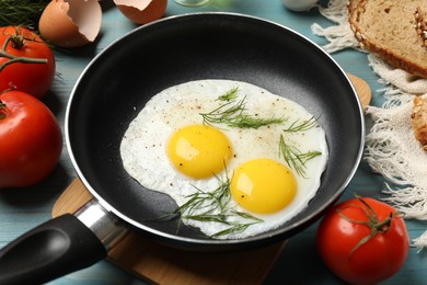 Photo of Frying pan with tasty cooked eggs, dill and other products on light blue wooden table