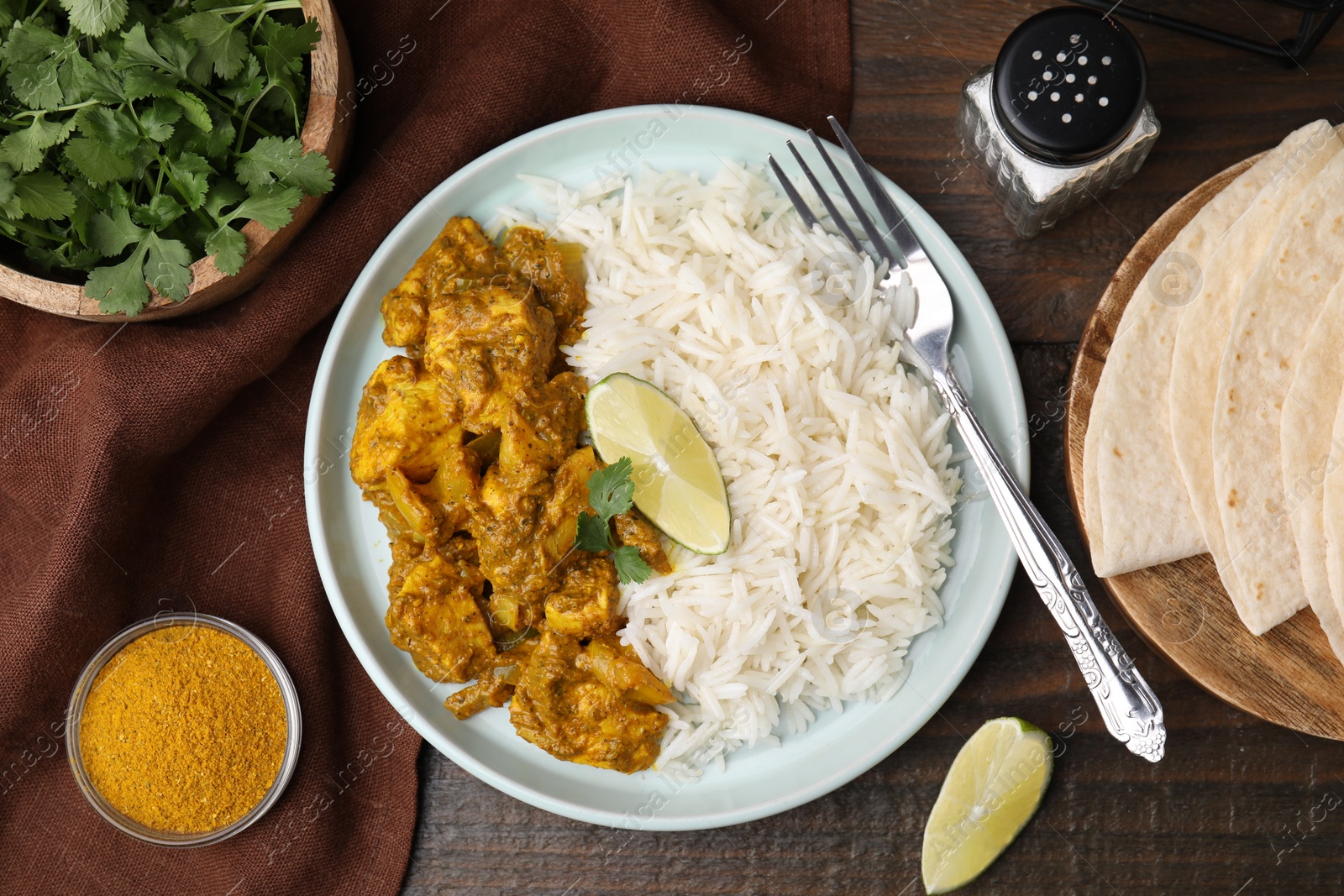 Photo of Delicious chicken curry with rice and ingredients on wooden table, flat lay