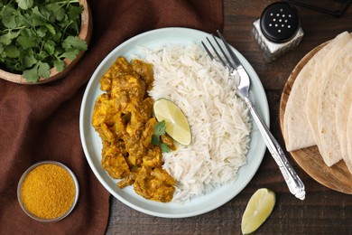 Photo of Delicious chicken curry with rice and ingredients on wooden table, flat lay