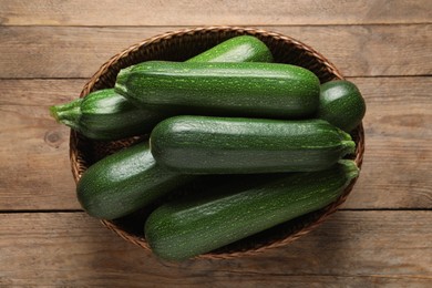 Photo of Raw ripe zucchinis in wicker basket on wooden table, top view