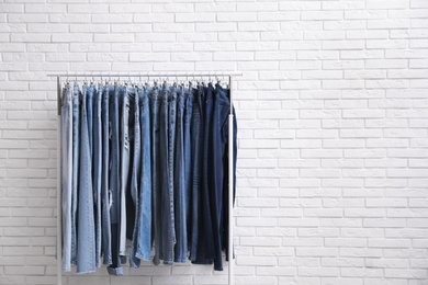 Rack with stylish jeans near brick wall. Space for text