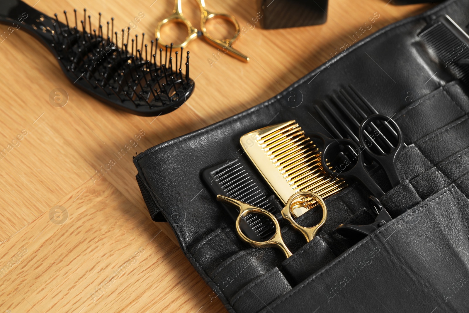 Photo of Hairdresser tools. Professional scissors and combs in leather organizer on wooden table, closeup