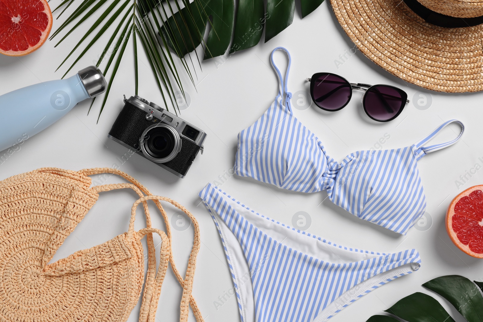 Photo of Beach bag, camera, leaves and accessories on white background, flat lay