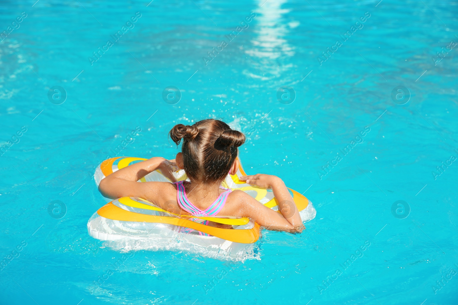 Photo of Little girl with inflatable ring in swimming pool on sunny day