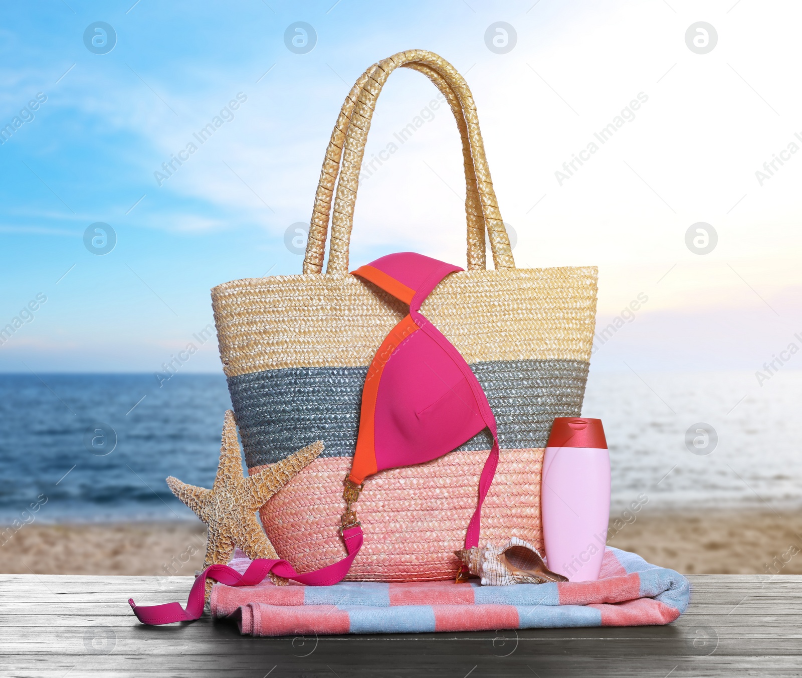 Image of Stylish bag and other beach accessories on wooden table near sea