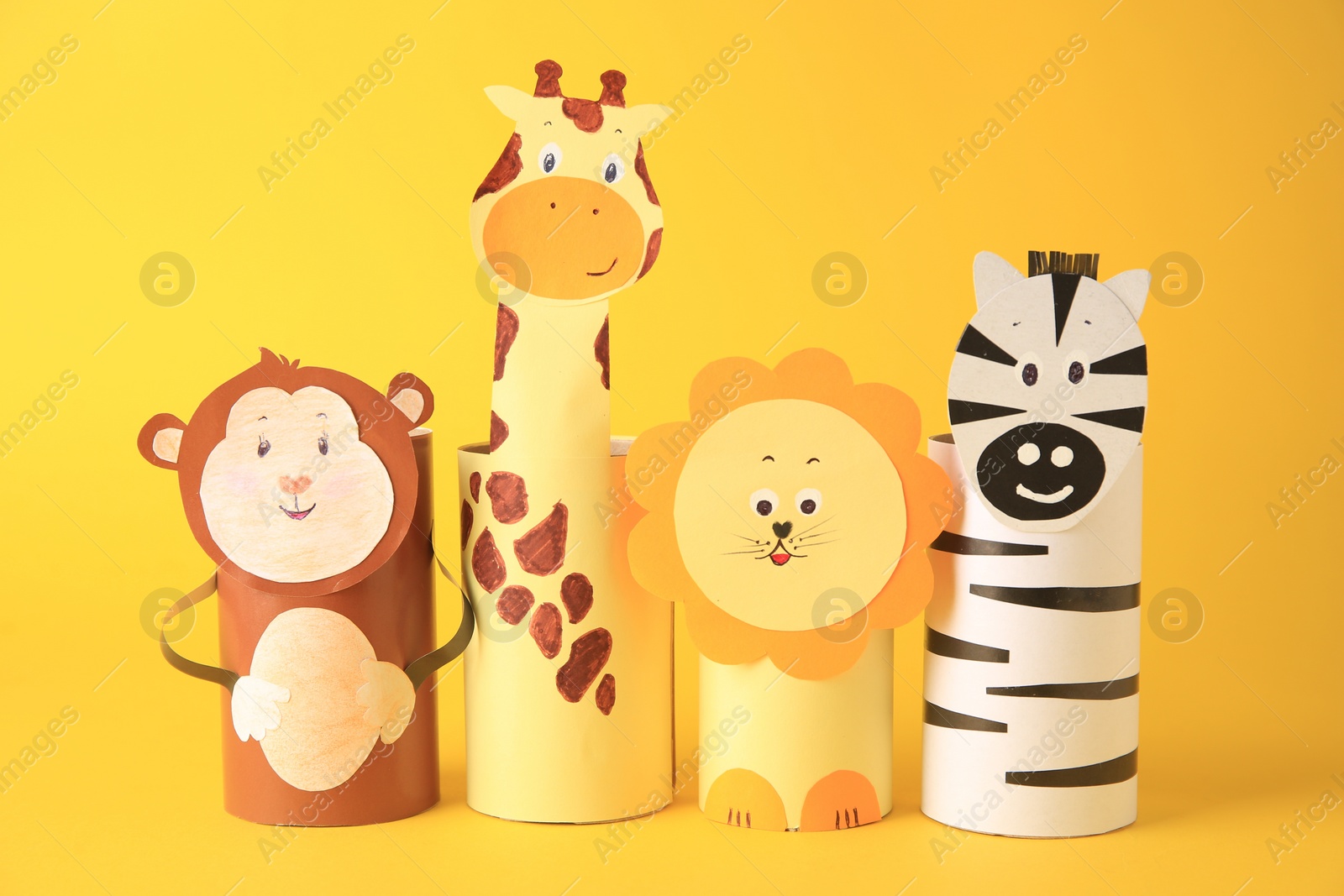 Photo of Toy monkey, giraffe, lion and zebra made from toilet paper hubs on yellow background. Children's handmade ideas