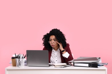 Stressful deadline. Scared woman looking at laptop at white desk on pink background