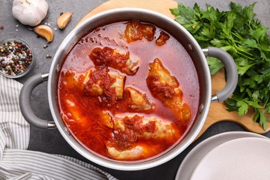 Delicious stuffed cabbage rolls cooked with homemade tomato sauce in pot and ingredients on grey table, flat lay