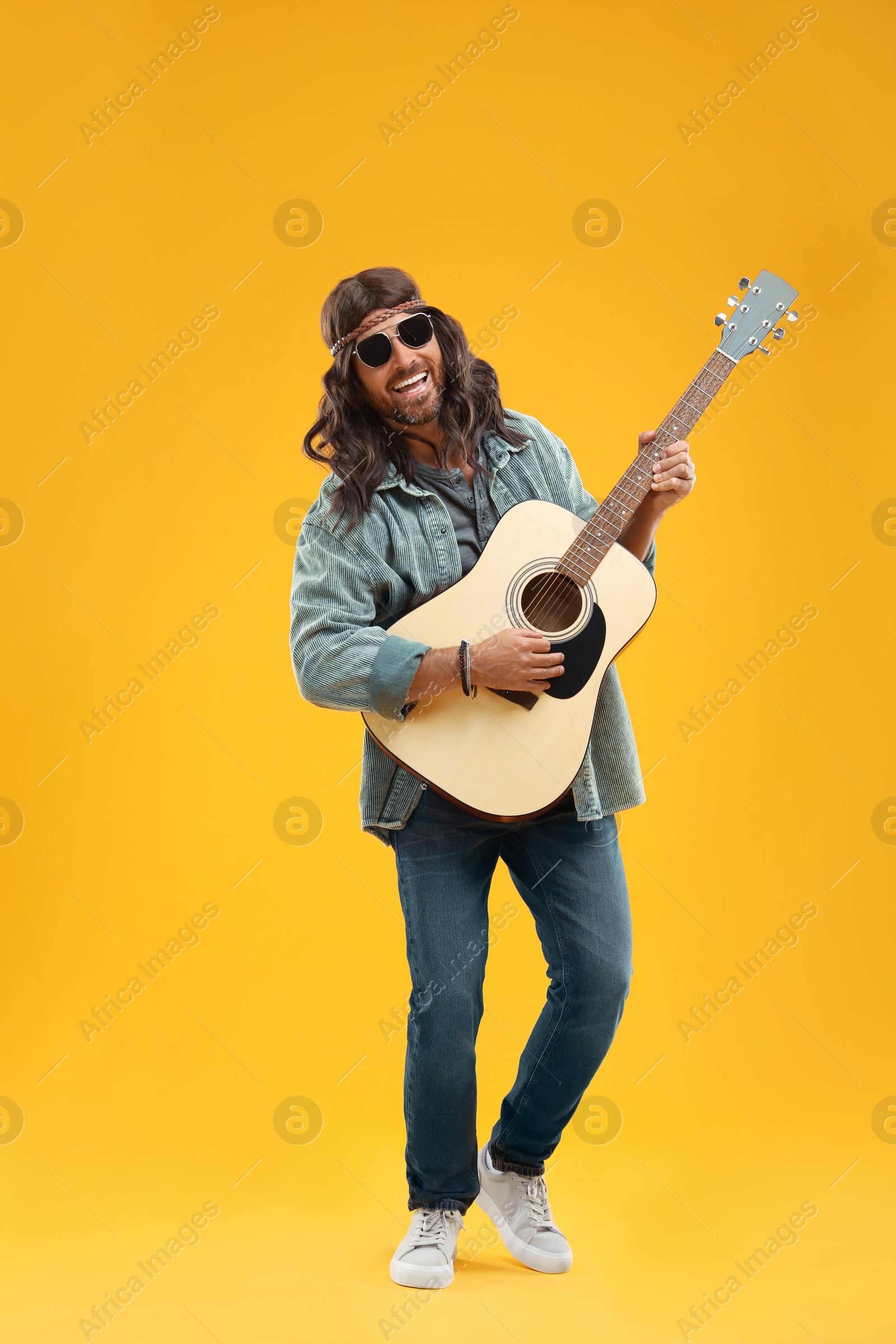 Photo of Stylish hippie man playing guitar on orange background