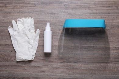 Photo of Face shield, medical gloves and antiseptic on wooden background, flat lay. Personal safety equipment