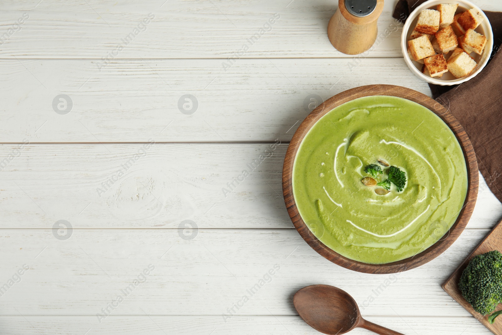 Photo of Delicious broccoli cream soup served on white wooden table, flat lay. Space for text