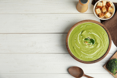 Delicious broccoli cream soup served on white wooden table, flat lay. Space for text