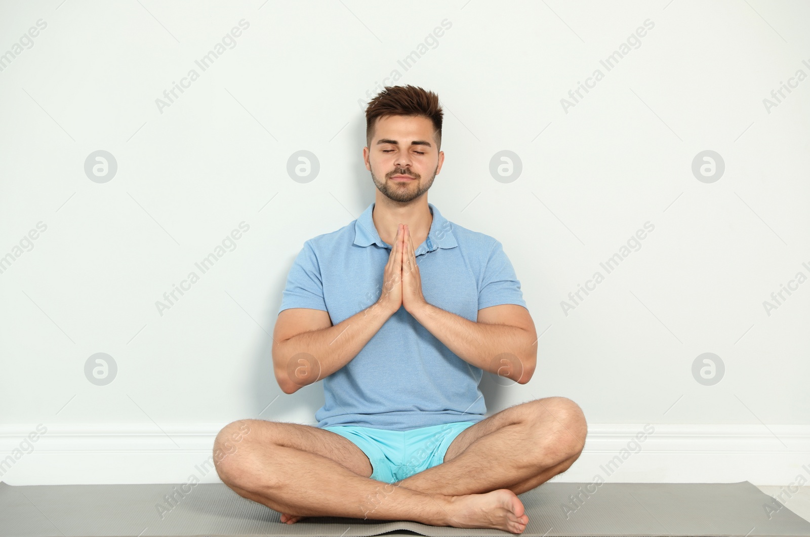 Photo of Young man practicing zen yoga near wall indoors