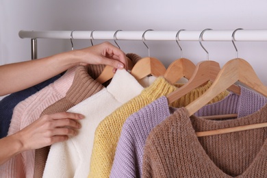 Photo of Woman choosing sweater on rack against white background, closeup
