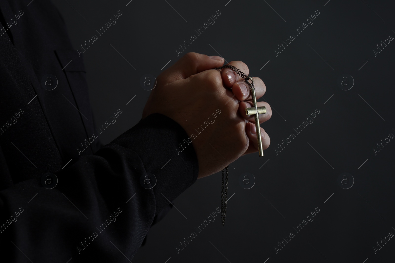 Photo of Priest with cross praying on black background, closeup