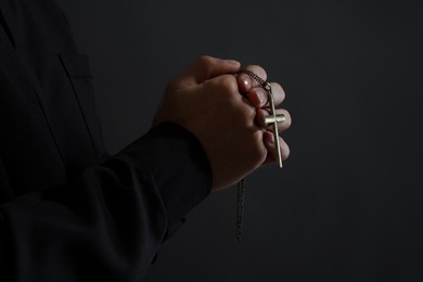 Priest with cross praying on black background, closeup