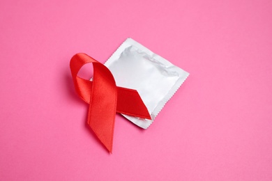 Photo of Red ribbon and condom on pink background, closeup. AIDS disease awareness