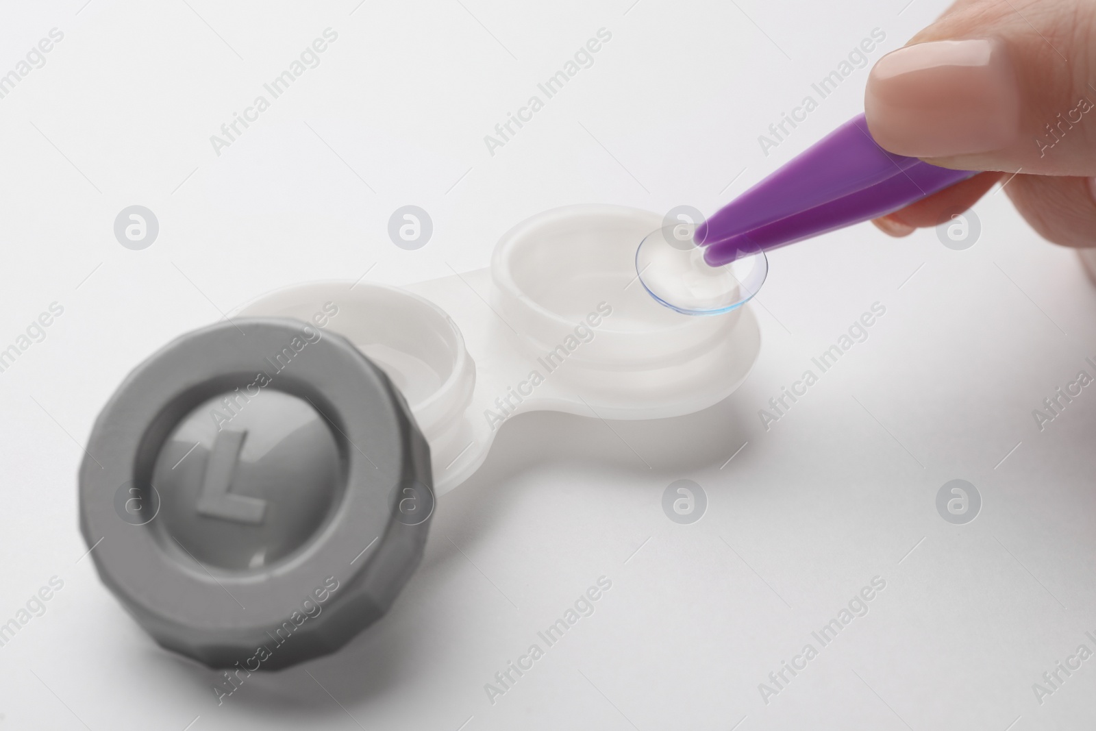 Photo of Woman taking contact lens from case with tweezers on white background, closeup