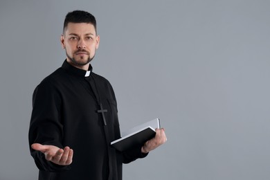 Photo of Priest with Bible praying on grey background, space for text