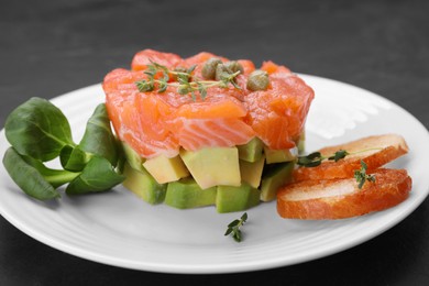 Delicious salmon tartare served with croutons, capers and greens on black table, closeup