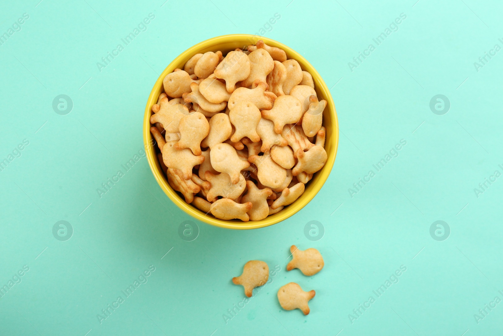 Photo of Delicious goldfish crackers in bowl on turquoise background, flat lay