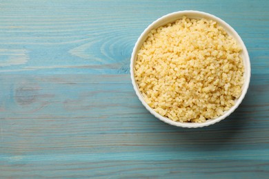 Photo of Delicious bulgur in bowl on light blue wooden table, top view. Space for text