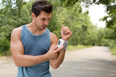 Young man checking pulse with medical device after training in park. Space for text