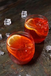 Photo of Aperol spritz cocktail, ice cubes and orange slices in glasses on grey textured table