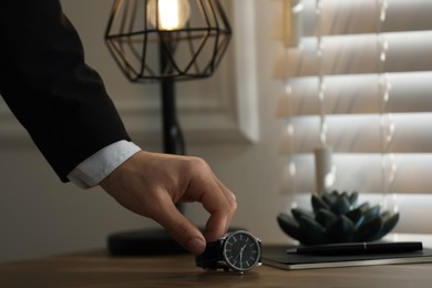 Man putting luxury wrist watch on table, closeup. Space for text