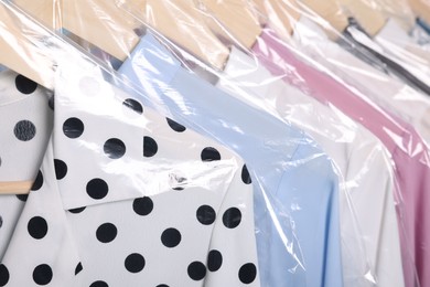 Photo of Dry-cleaning service. Many different clothes in plastic bags hanging on rack, closeup