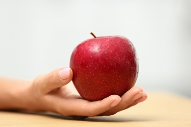 Photo of Woman holding fresh red apple at table, closeup