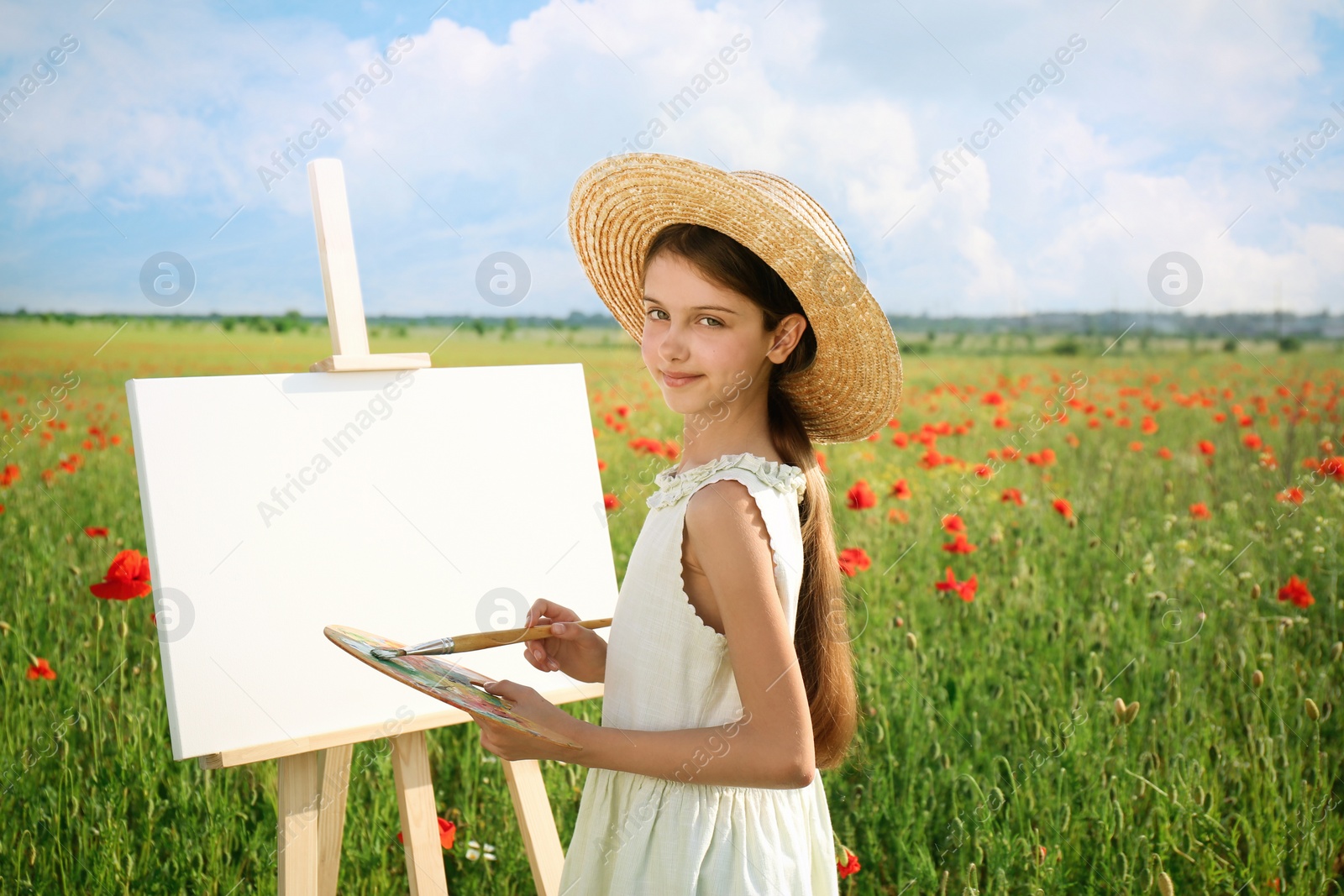 Photo of Little girl painting on easel in beautiful poppy field