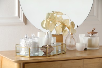 Photo of Containers with cotton swabs, pads and burning candle near cosmetic products on dressing table