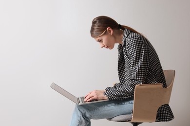 Photo of Woman with bad posture using laptop while sitting on chair against light grey background, space for text