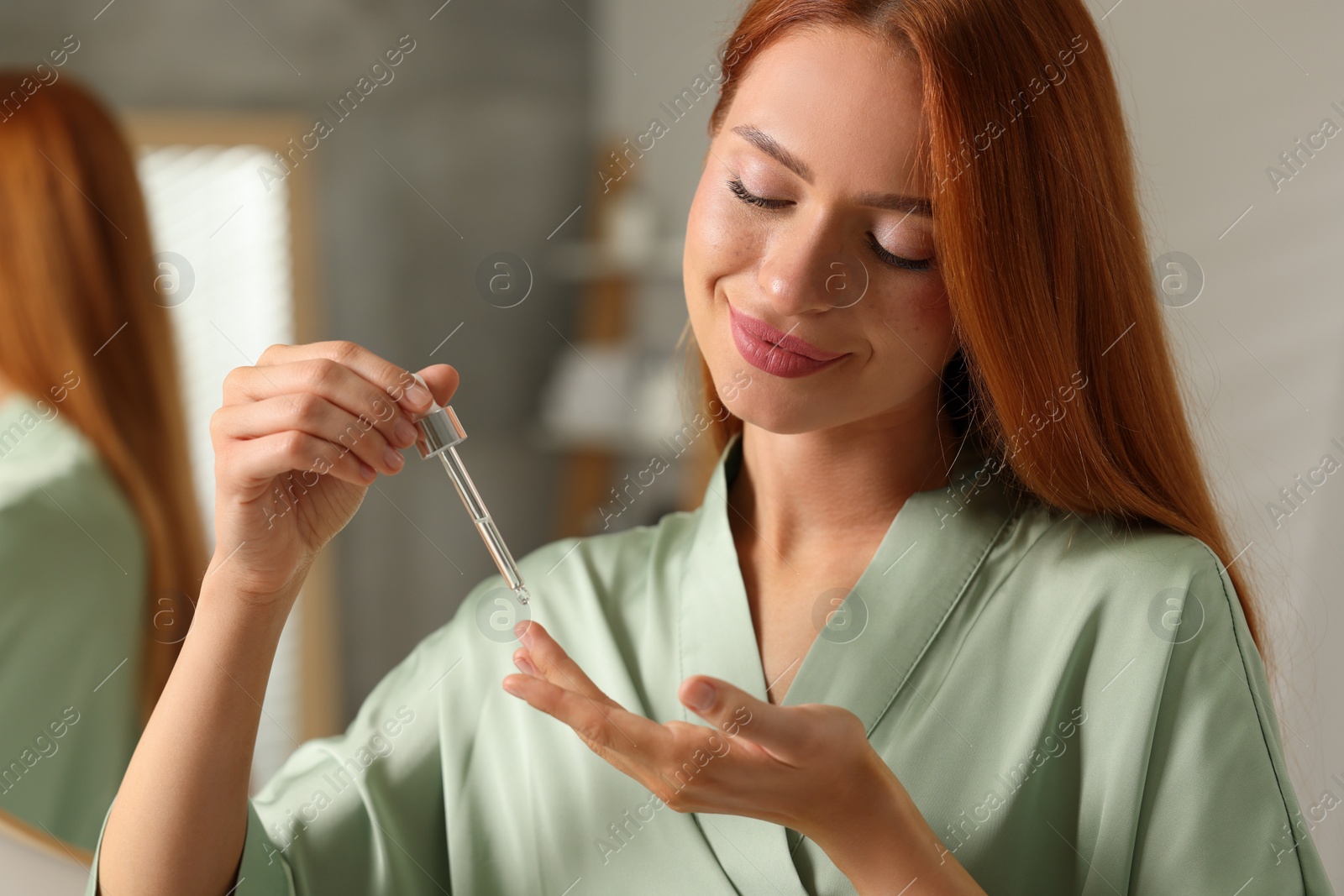 Photo of Beautiful young woman applying cosmetic serum onto her finger in bathroom, closeup