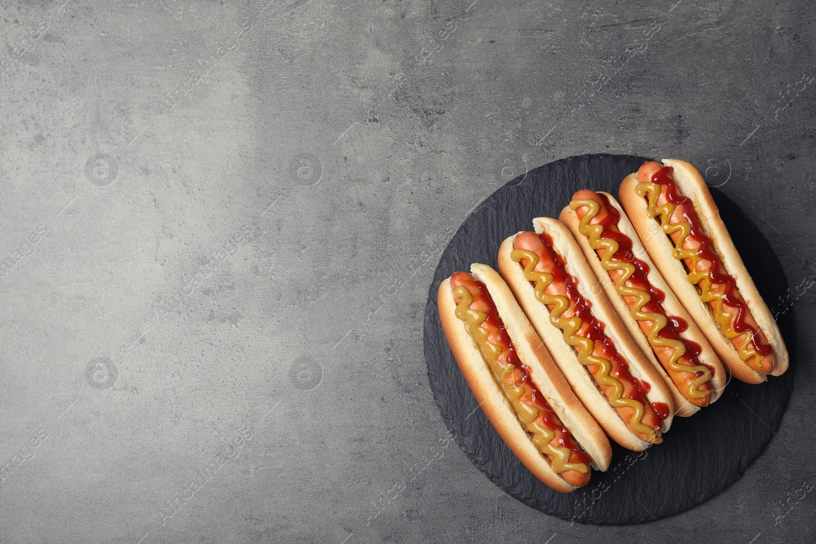 Photo of Slate plate with hot dogs on grey background, top view. Space for text