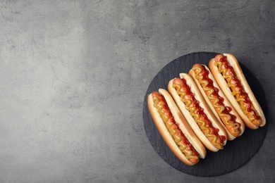 Photo of Slate plate with hot dogs on grey background, top view. Space for text