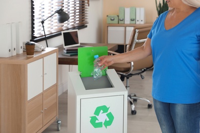 Woman throwing plastic bottle into recycling bin at office, closeup