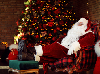 Photo of Santa Claus resting in armchair near decorated Christmas tree indoors