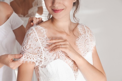 Photo of Woman helping bride to put on wedding dress indoors, closeup